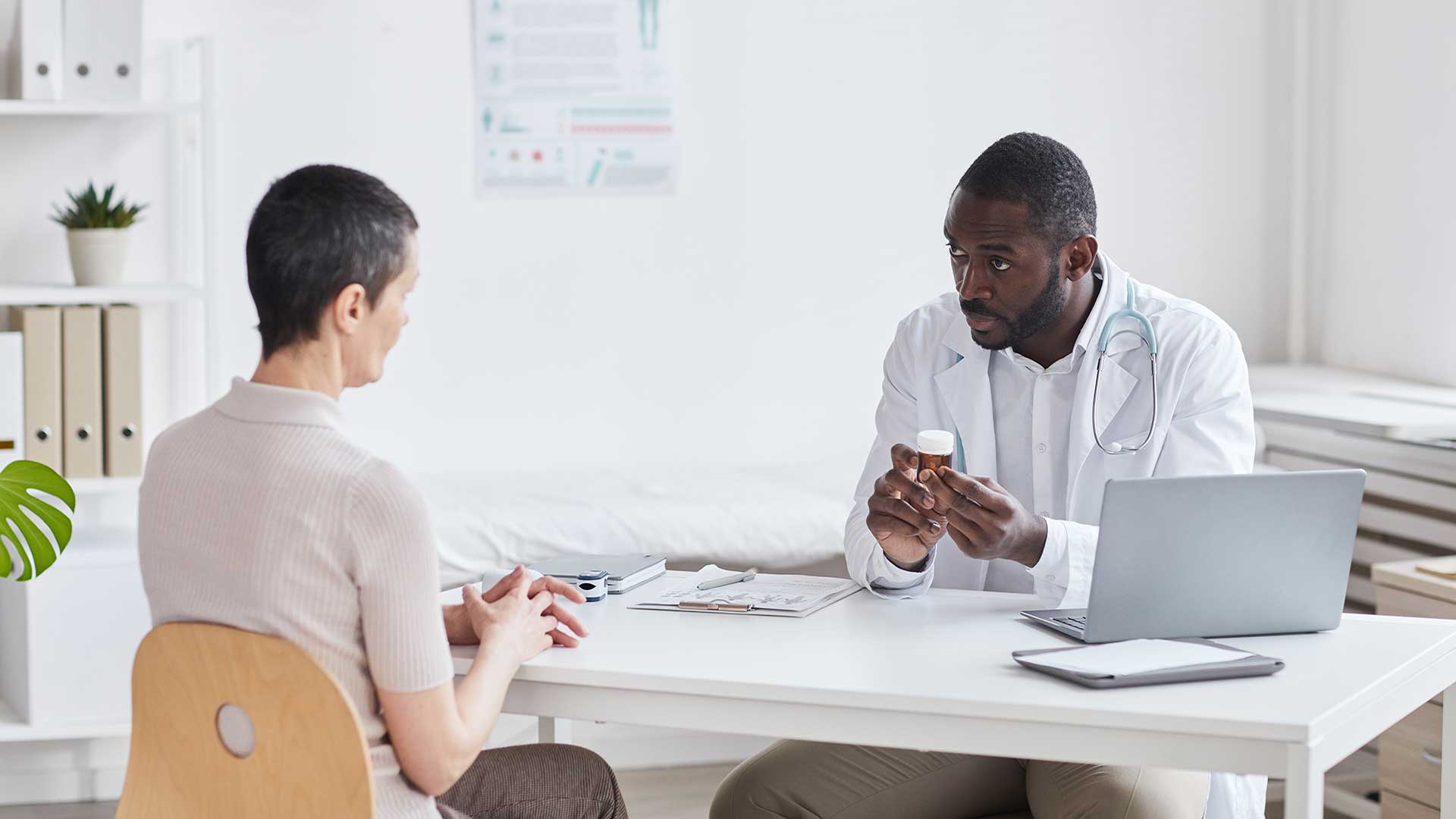 Male physician holding pill bottle talking to female patient